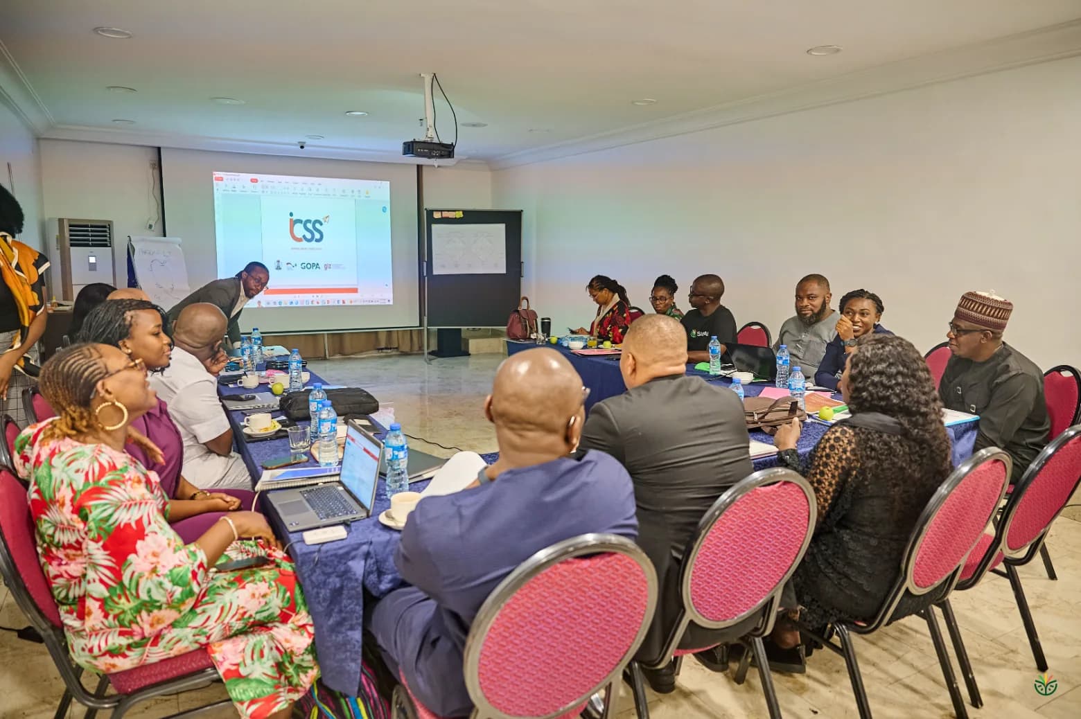 The workshop room: founders, trainers and officials around a U-shaped table, ICSS on the screen